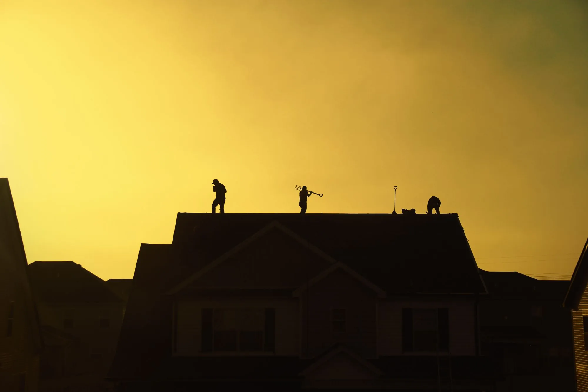 Roofers silhouetted along a roof ridge against an evening sky