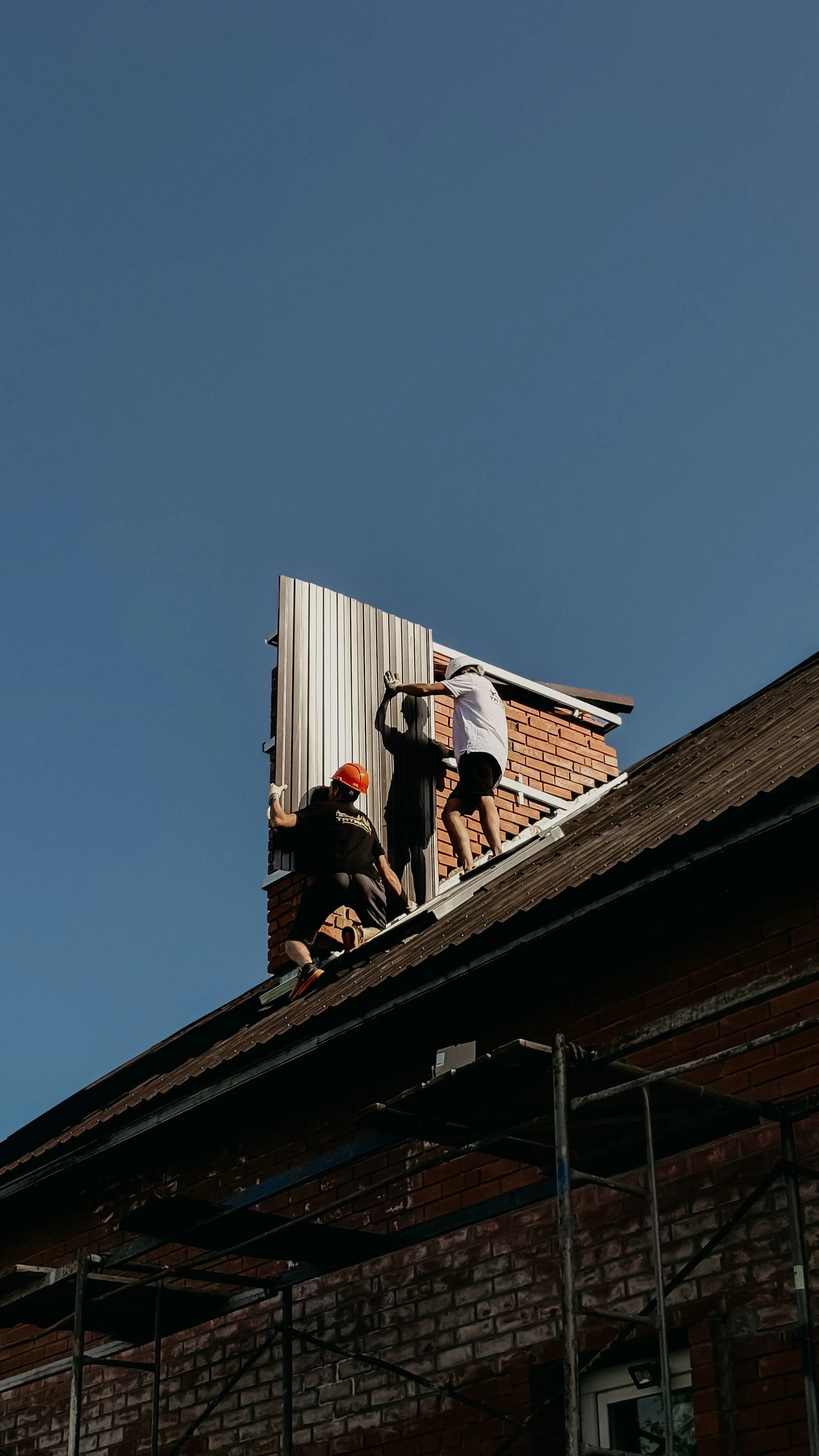 Two roofers working at a roof edge with a ladder