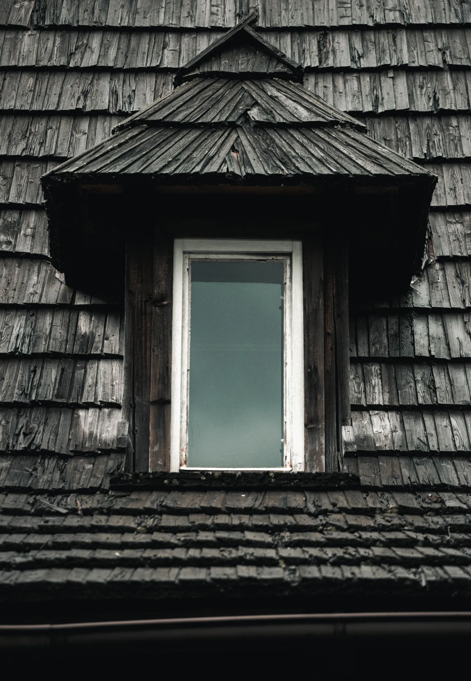 Weathered shingle siding around a window on a house wall